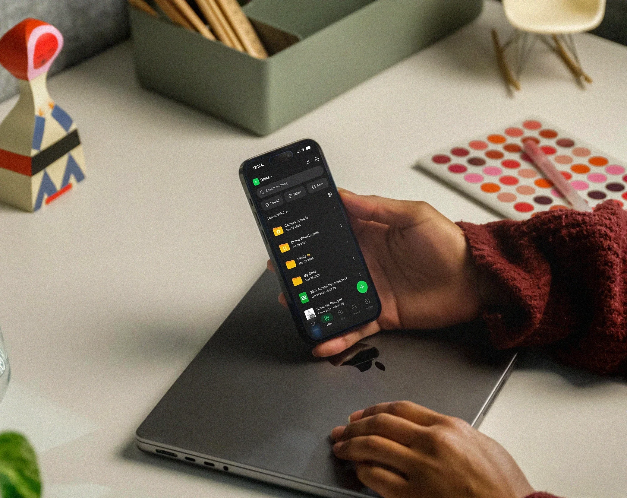 Smartphone mit der Drime-Dateiliste im dunklen Modus, über einen Laptop gehalten
