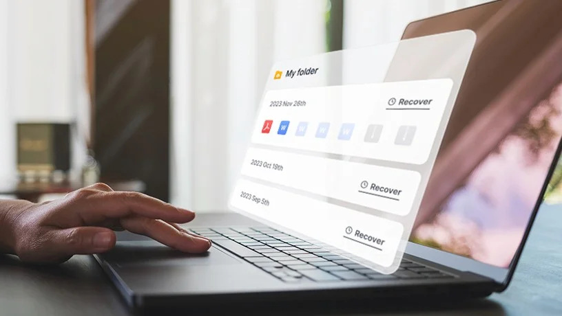 Ordinateur portable avec un panneau « My folder » listant des versions datées, chacune avec un bouton Recover